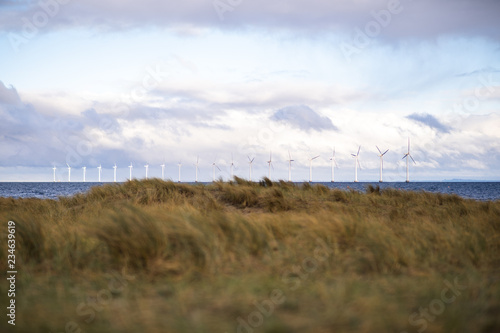 wind turbine out in water at amager beach in denmark, with grass in the fourground © Lars