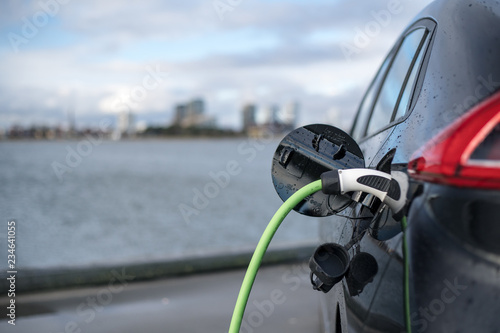 Charging an electric car, with the city and water in the background, green charging cable and black car. copenhagen