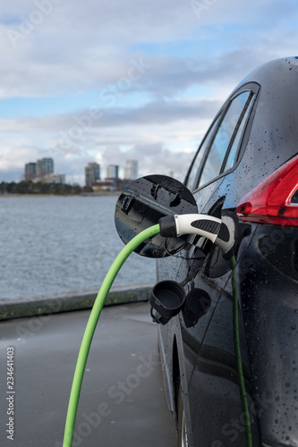 Charging an electric car, with the city and water in the background, green charging cable and black car. copenhagen