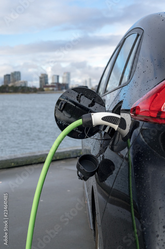 Charging an electric car, with the city and water in the background, green charging cable and black car. copenhagen