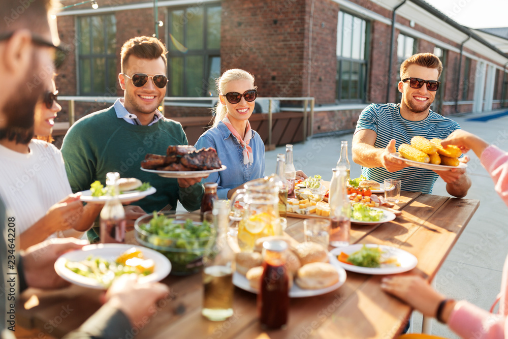 leisure and people concept - happy friends eating and drinking at barbecue party on rooftop in summer leisure and people concept - happy friends eating and drinking at barbecue party on rooftop in summer