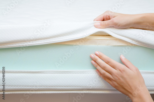 Woman's hands touching different layers of new mattress. Checking hardness and softness. Choice of the best type and quality. Front view. Close up. photo