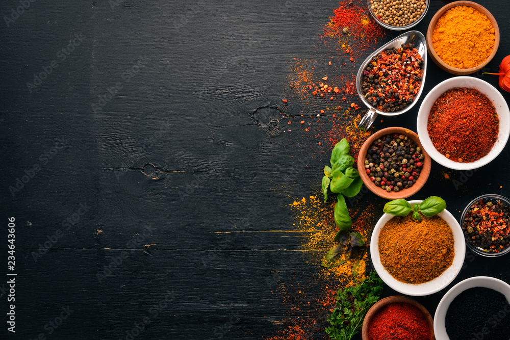 Spices and herbs on a wooden board. Pepper, salt, paprika, basil, turmeric. On a black wooden chalkboard. Top view. Free copy space. - obrazy, fototapety, plakaty 
