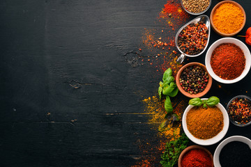 Spices and herbs on a wooden board. Pepper, salt, paprika, basil, turmeric. On a black wooden chalkboard. Top view. Free copy space.