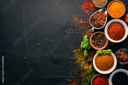 Spices and herbs on a wooden board. Pepper, salt, paprika, basil, turmeric. On a black wooden chalkboard. Top view. Free copy space.