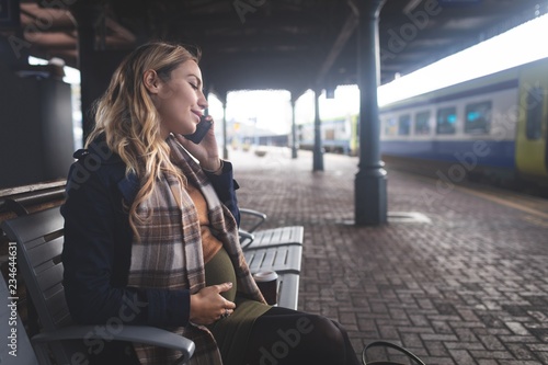 Pregnant woman talking on mobile phone at railway station photo