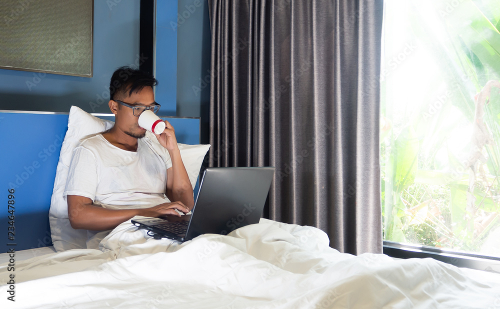 Asian business man have beard siting in the bed in the morning, Work on notebook in his lap, at the same time drink coffee, Concept working on the bed. Asian business man have beard siting in the bed in the morning, Work on notebook in his lap, at the same time drink coffee, Concept working on the bed.
