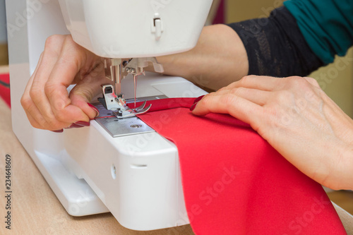 Woman's hands working with sewing machine. Making new, modern, classic dress, blouse, trousers or other clothes. Red fabric. Handmade work. Feminine hobby. Closeup.