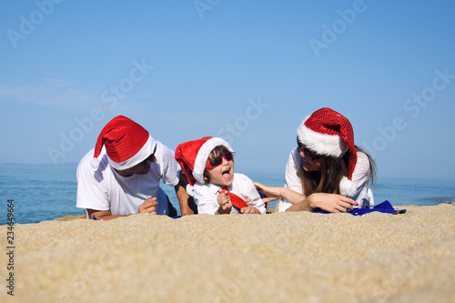 Happy family in Christmas Hats having fun on sandy beach. New Year holidays concept