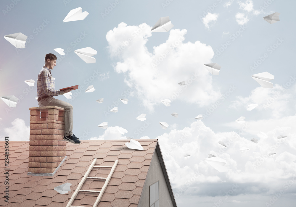 Man on brick roof reading book and paper planes flying in air Man on brick roof reading book and paper planes flying in air