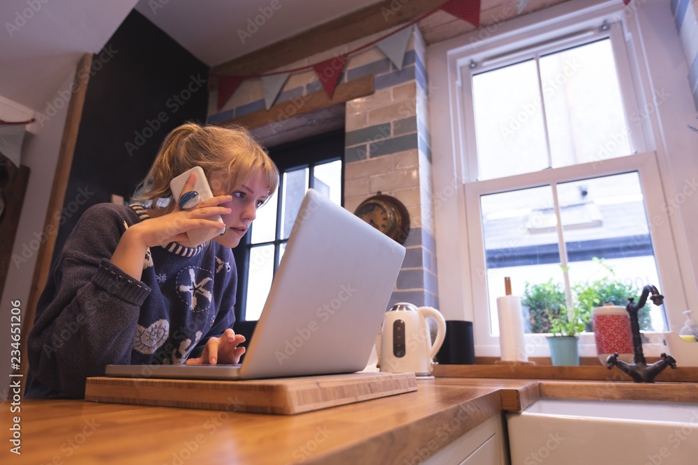 Woman talking on mobile phone while using laptop at home Woman talking on mobile phone while using laptop at home