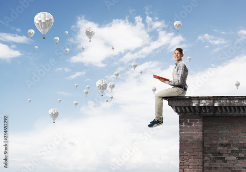 Man on roof edge reading book and aerostats flying in sky © adam121