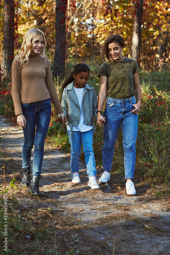 A beautiful couple of lesbian ladies having a walk in the autumn park with  their adopted teenage daughter. The young family walking, holding hands,  chatting, smiling. The girls wearing casual outfit. foto