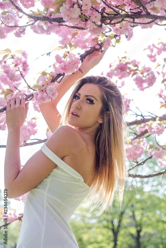 Sensual woman in white dress holding flowering cherry branch in park Sensual woman in white dress holding flowering cherry branch in park