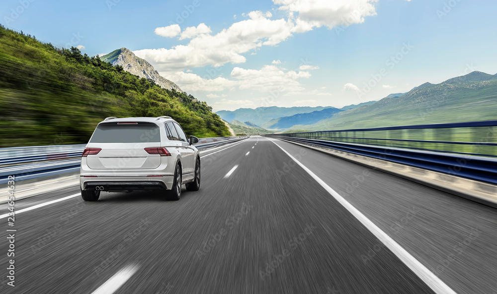Fototapeta premium Biały samochód pędzący wzdłuż szybkiej autostrady w słońcu.