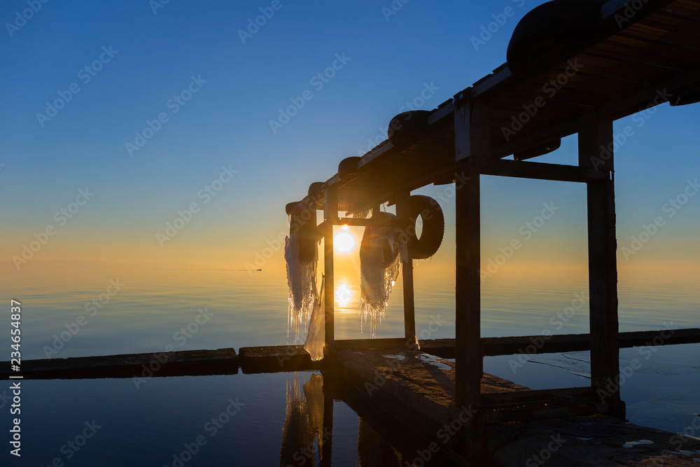 Sunset sea view with wooden ice-covered pier.