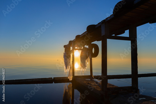 Sunset sea view with wooden ice-covered pier.