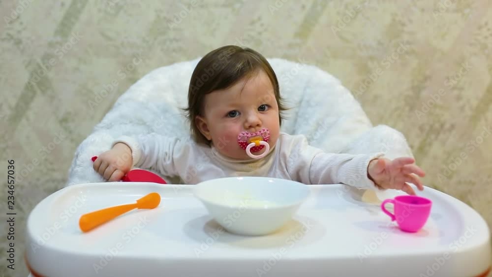 Cute toddler girl sitting in the child chair is ready to fed porridge with spoon by mother hand Cute toddler girl sitting in the child chair is ready to fed porridge with spoon by mother hand