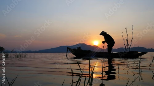 Silhouette scene of Fisherman on boat fishing with a fishnet. He use old traditional fishing equipment for fishing in The lake. Bang Phra Lake - Eastern of Thailand photo