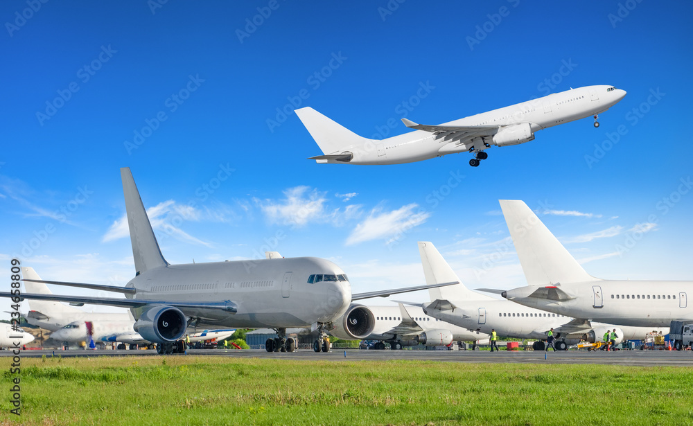 Several airplanes at the airport, one is flying in the sky. Several airplanes at the airport, one is flying in the sky.
