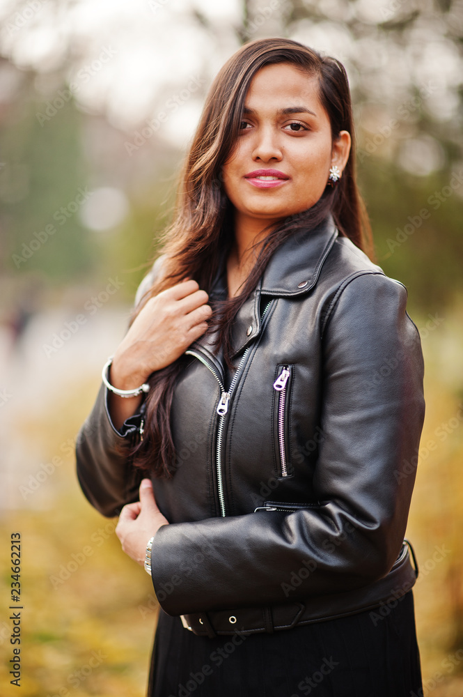 Close up portrait of pretty indian girl in black saree dress and leather jacket posed outdoor at autumn street. Stock Photo Adobe Stock