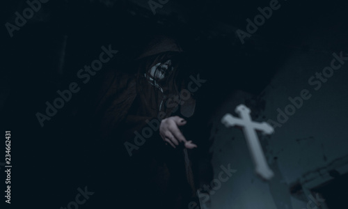 Woman is standing in a darkness next to the cross flying in the air in an image of a nun possessed by demons.