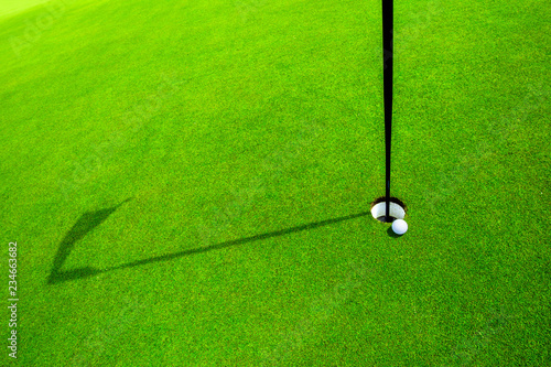 golf ball in the green grass close to the hole with the shadow of the flagpole