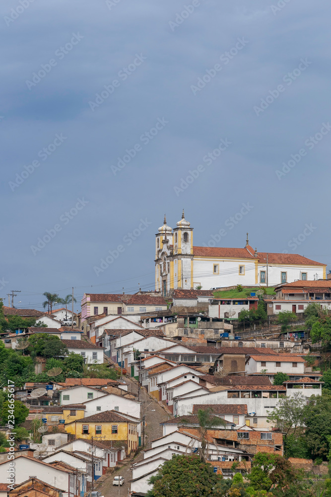 Igreja de Santa Ifigênia e casario alinhados ladeira abaixo na cidade histórica de Ouro Preto, Brasil.