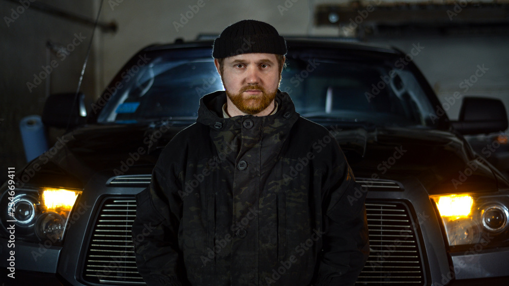 Portrait of a serious man with a beard in uniform near a pickup truck
