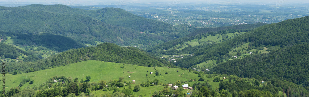 Mountains, green forests, pastures and a village in the Carpathians in summer, aerial view, panorama