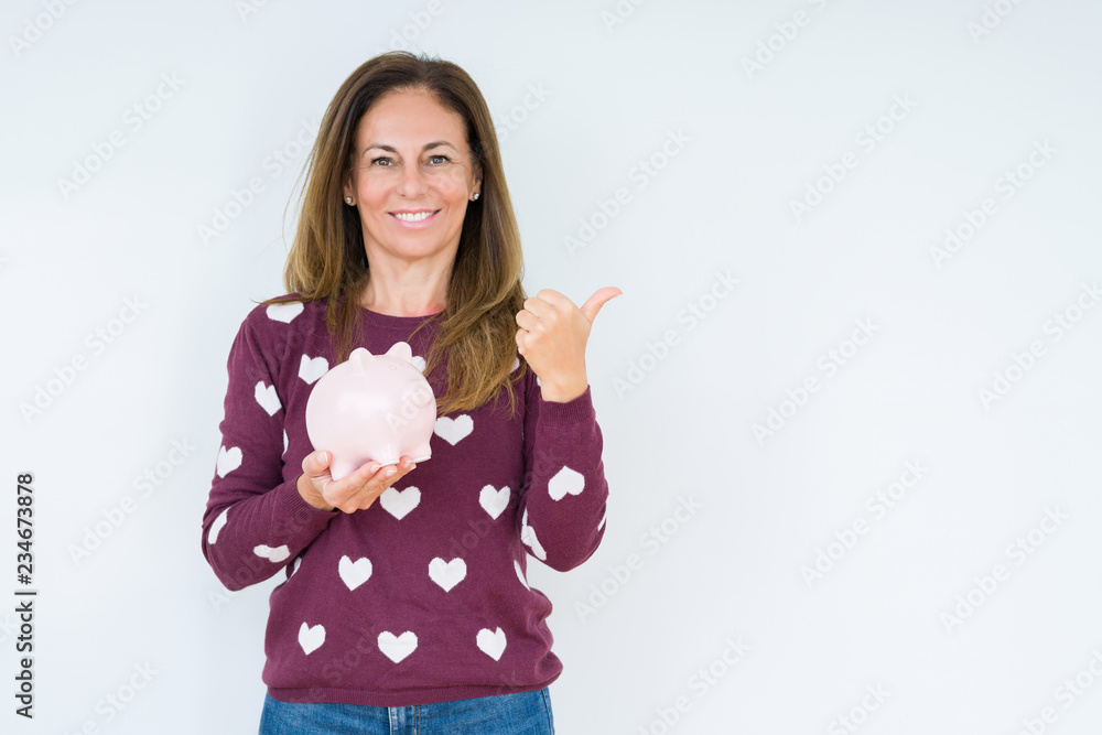 Middle age woman holding piggy bank over isolated background happy with big smile doing ok sign, thumb up with fingers, excellent sign Middle age woman holding piggy bank over isolated background happy with big smile doing ok sign, thumb up with fingers, excellent sign