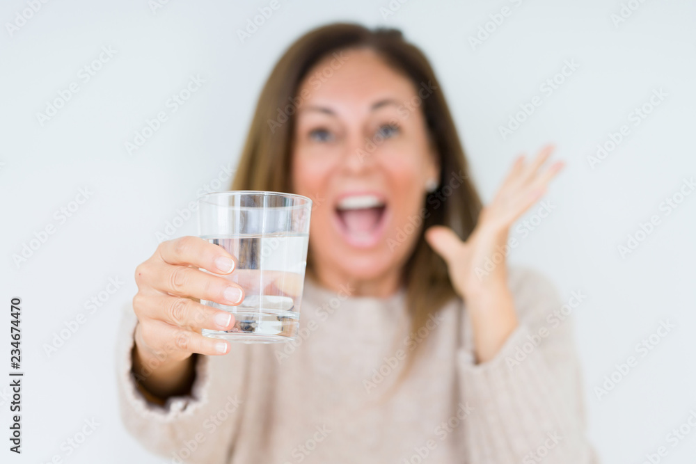Middle age woman drinking glass of water isolated background very happy and excited, winner expression celebrating victory screaming with big smile and raised hands Middle age woman drinking glass of water isolated background very happy and excited, winner expression celebrating victory screaming with big smile and raised hands
