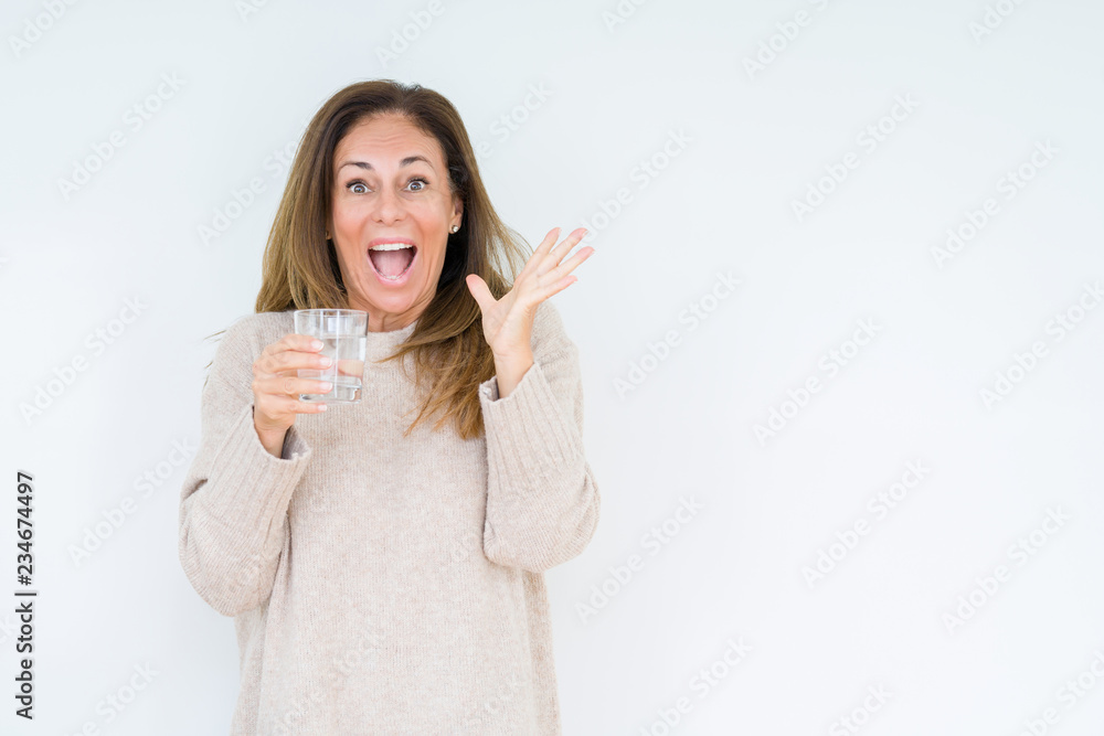 Middle age woman drinking glass of water isolated background very happy and excited, winner expression celebrating victory screaming with big smile and raised hands Middle age woman drinking glass of water isolated background very happy and excited, winner expression celebrating victory screaming with big smile and raised hands