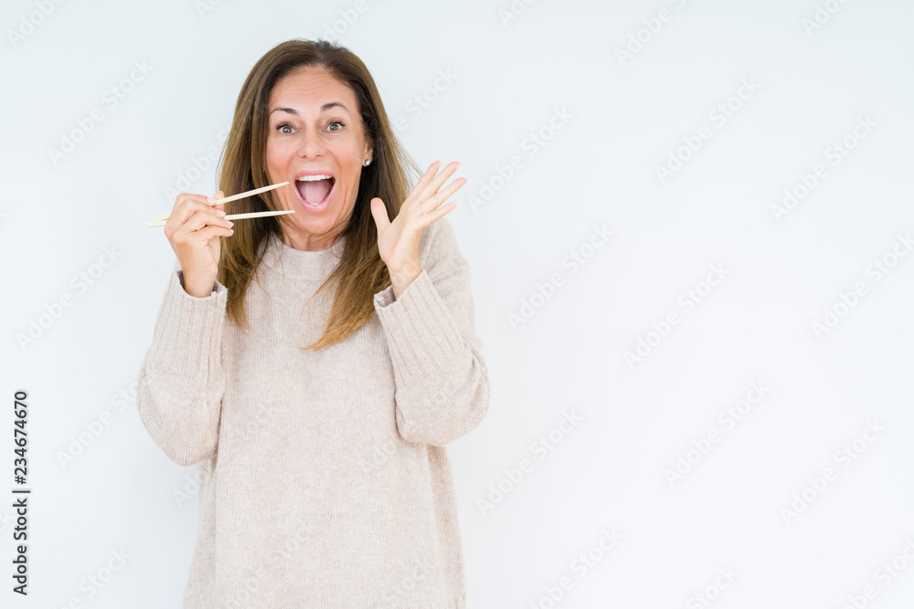 Middle age woman holding asian chopsticks over isolated background very happy and excited, winner expression celebrating victory screaming with big smile and raised hands Middle age woman holding asian chopsticks over isolated background very happy and excited, winner expression celebrating victory screaming with big smile and raised hands