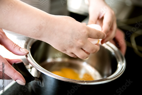 A child helps mom cook breakfast and breaks eggs into a saucepan. 
