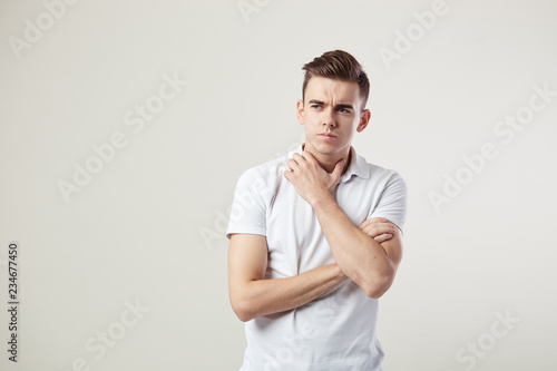 Thoughtful guy dressed in a white t-shirt and jeans is on a white background in the studio