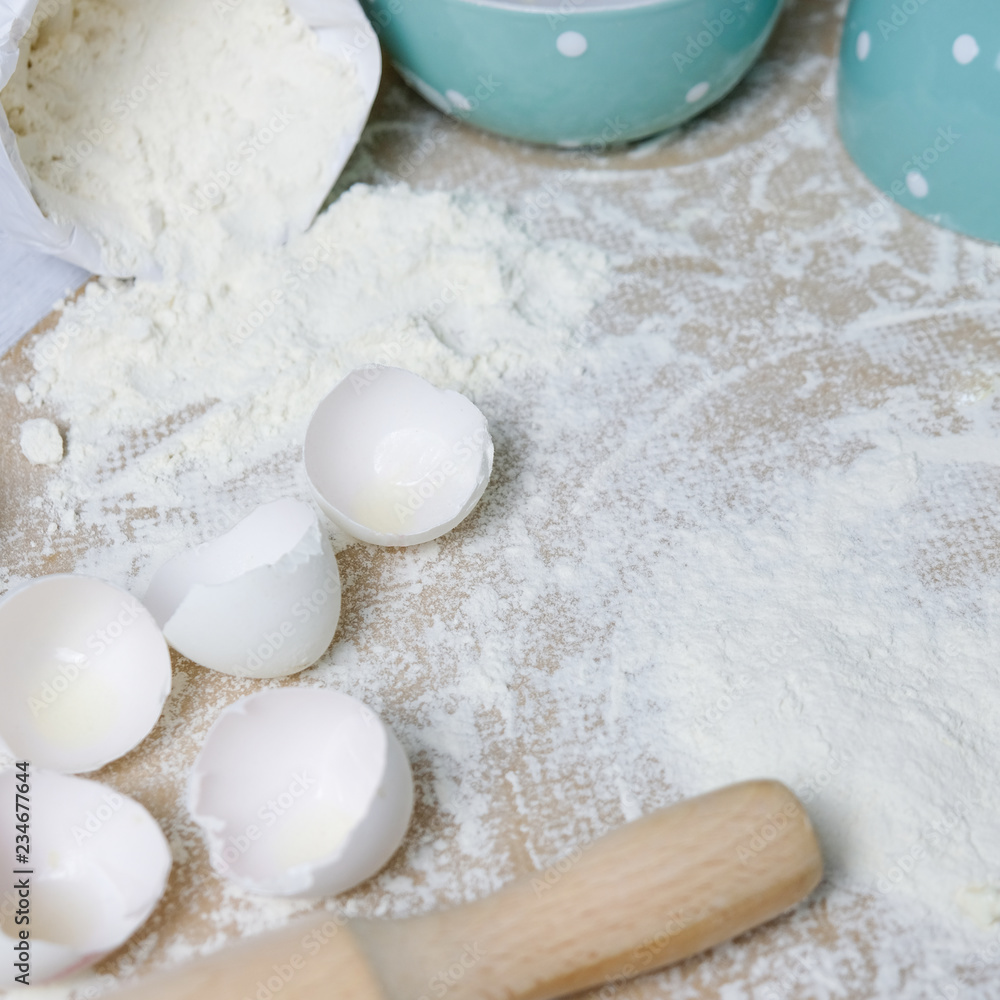 Table with ingredients for dough, raw eggs, flour, plate, napkins, rolling pin. Process of preparing pie, kitchen objects, flat lay with light white and blue colors space for text Table with ingredients for dough, raw eggs, flour, plate, napkins, rolling pin. Process of preparing pie, kitchen objects, flat lay with light white and blue colors space for text