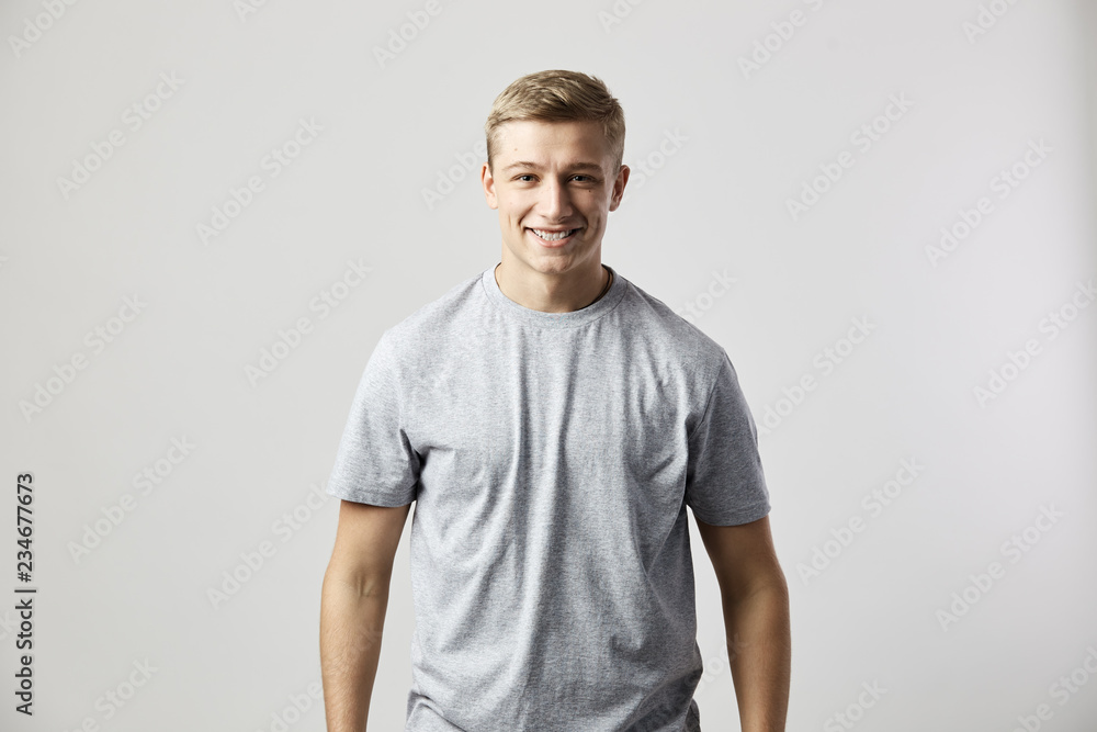 Smiling guy dressed in a white t-shirt stands on the white background in the studio Smiling guy dressed in a white t-shirt stands on the white background in the studio