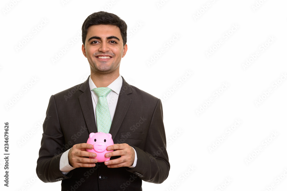 Young happy Persian businessman holding piggy bank Young happy Persian businessman holding piggy bank