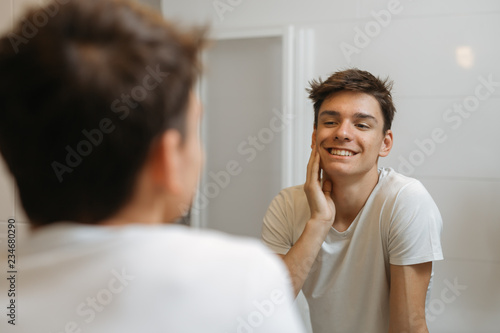 teenage boy looking at his face in bathroom. skin problem concept