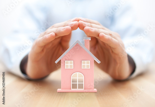 Property insurance. House miniature covered by hands. 