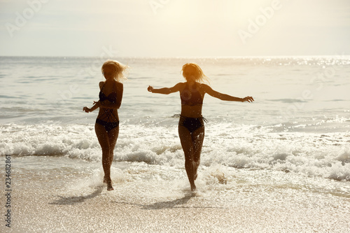 Two happy girls runs tropical sea beach