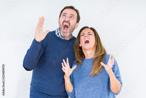 Beautiful middle age couple in love over isolated background crazy and mad shouting and yelling with aggressive expression and arms raised. Frustration concept.