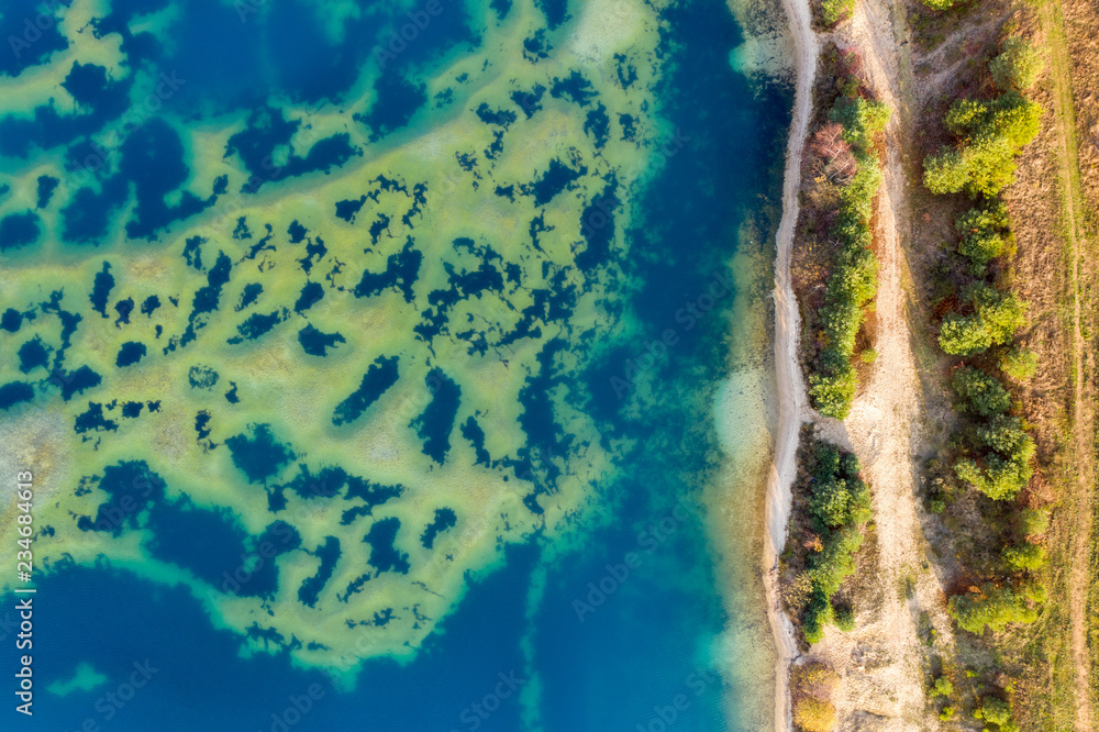 Abstract aerial image of a deep blue gravel lake with sandbanks almost reaching the surface of the water.