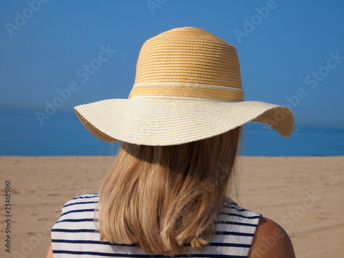 Young girl with hat on the beach. Back view.