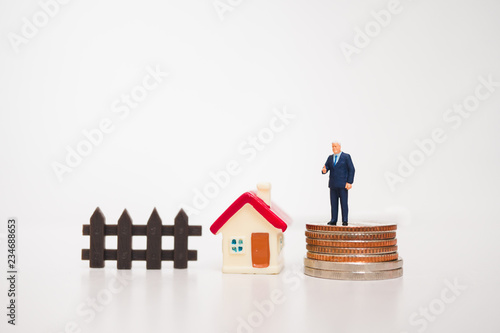 Miniature people, businessman standing on coins with mini house isolated on white background using as business concept