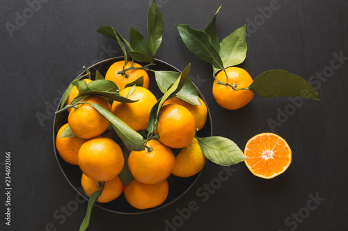Fresh mandarins with leaves in bowl on black. Healthy eating concept. Copy space.