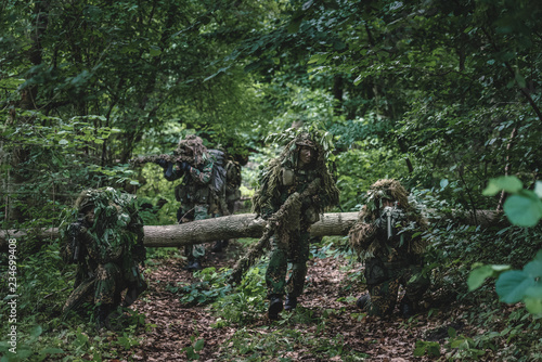 Camouflaged soldiers in forest during summer on patrol 