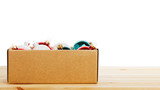 Cardboard box with colorful glass Christmas balls on wooden table against white background. Copyspace.