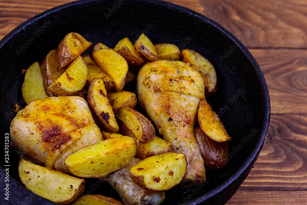 Baked chicken drumsticks with potatoes in cast-iron frying pan on wooden table Baked chicken drumsticks with potatoes in cast-iron frying pan on wooden table